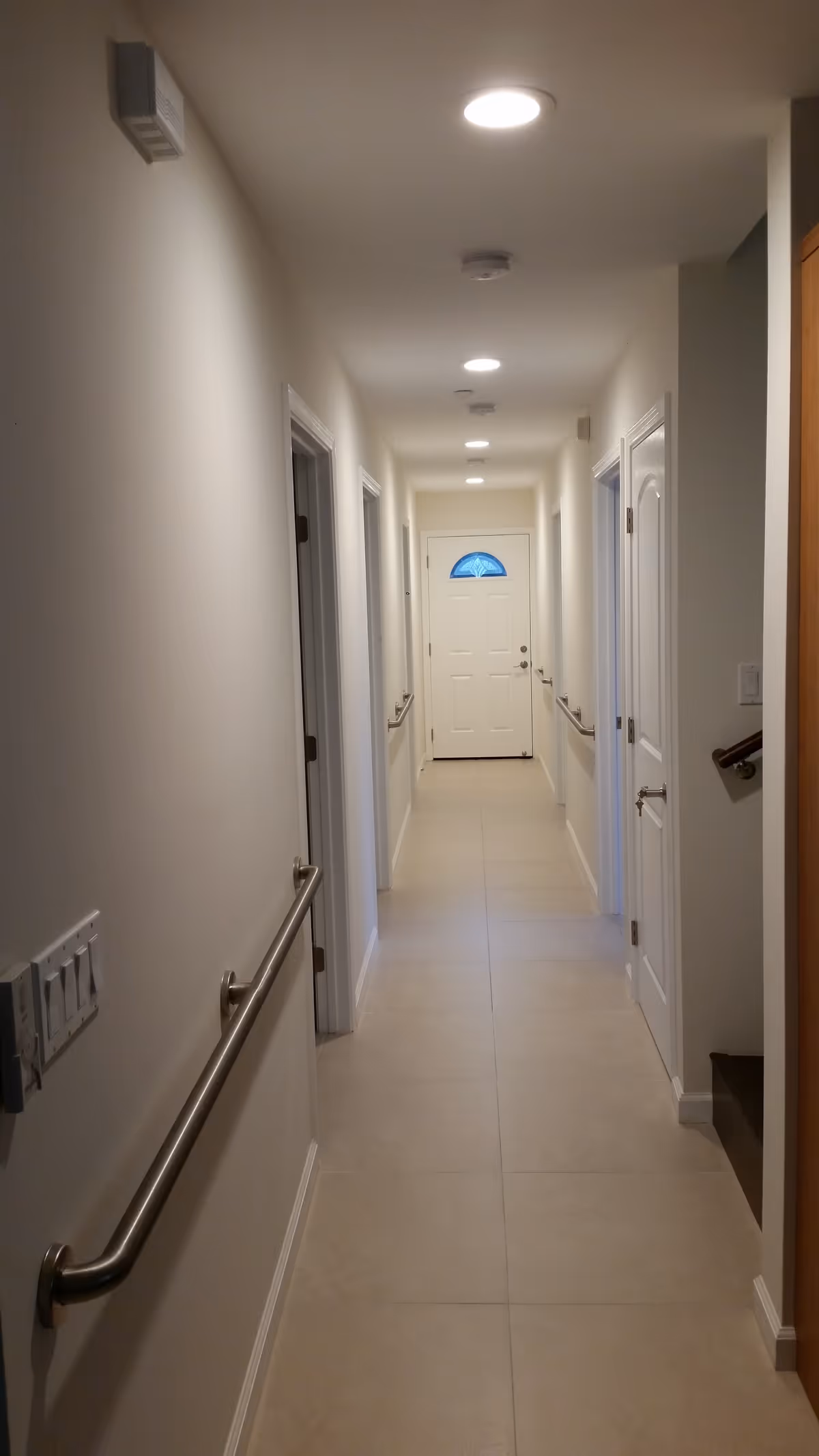 Long, well-lit interior hallway with handrails on both sides and a white door with a semicircular window at the far end.
