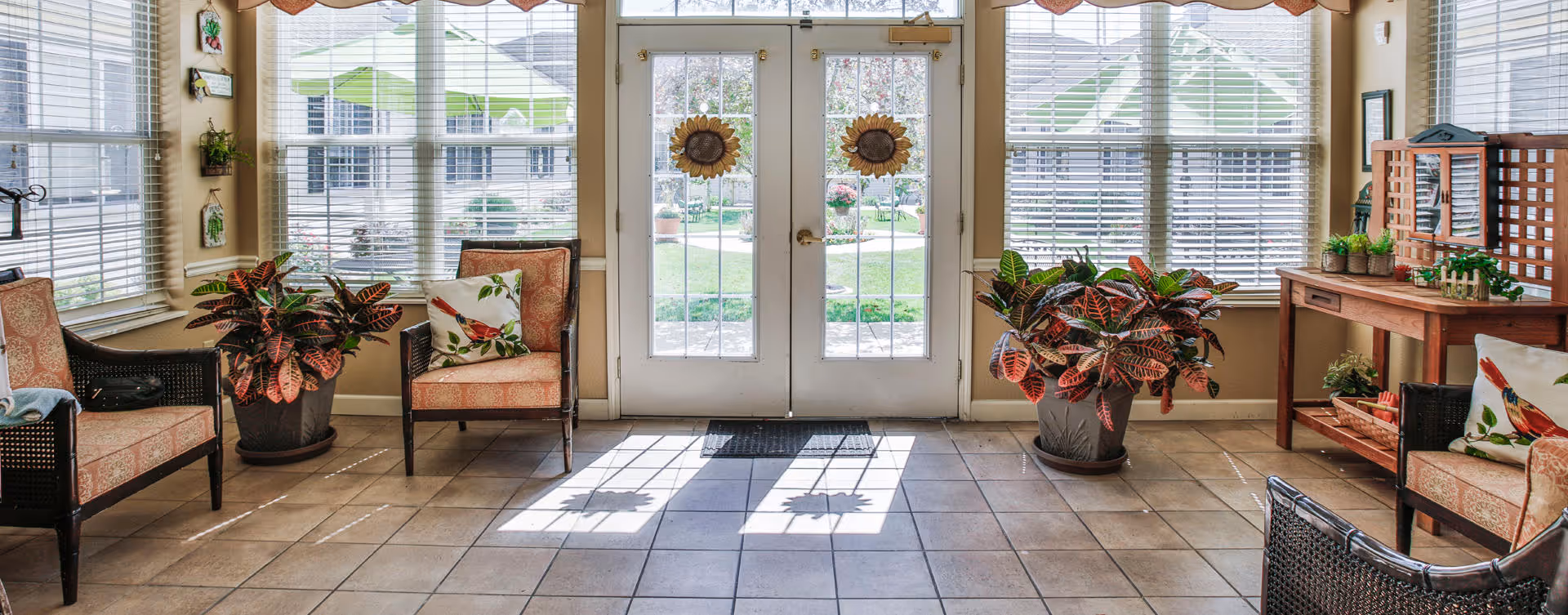 Bright seating area with wicker chairs, potted plants, and double glass doors opening to a courtyard.