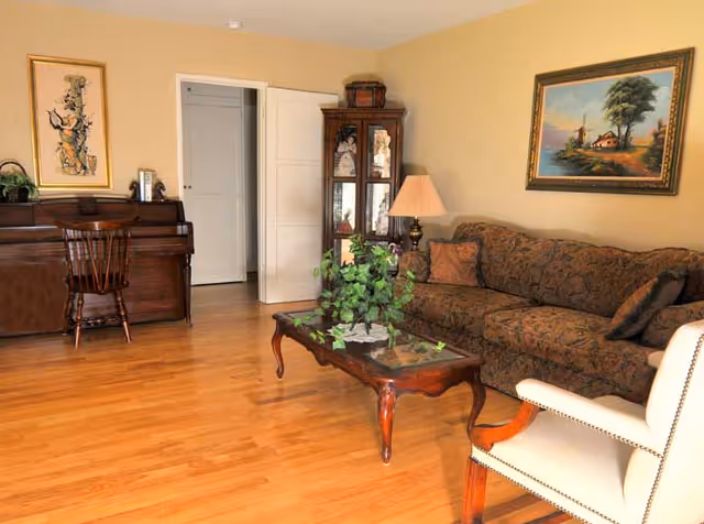 Cozy living room with a brown patterned sofa, glass coffee table, piano, and wall art.