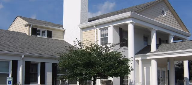 White multi-story senior living facility with columns and a tree in front.
