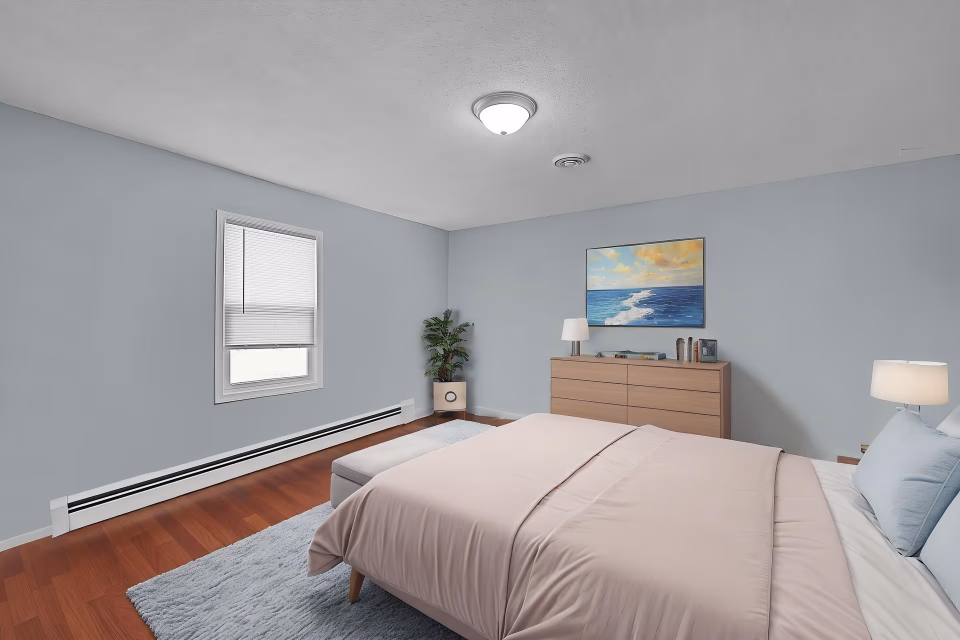 Bedroom with a neatly made bed, dresser with lamps and a seascape painting, a window, potted plant, and hardwood floor.