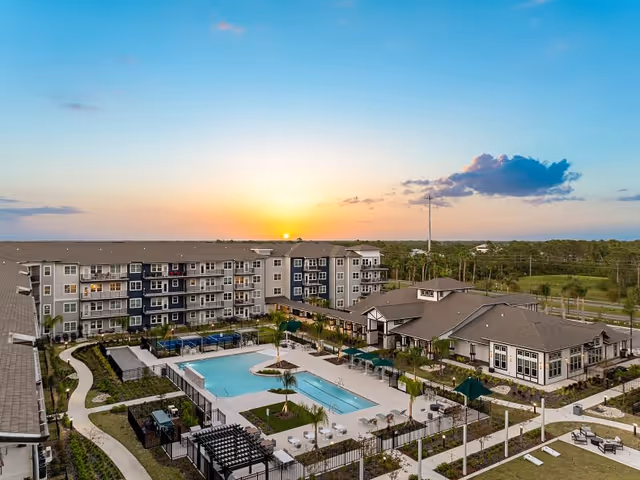 Aerial view of a multi-story senior living complex with a central swimming pool and landscaped courtyards at sunset.