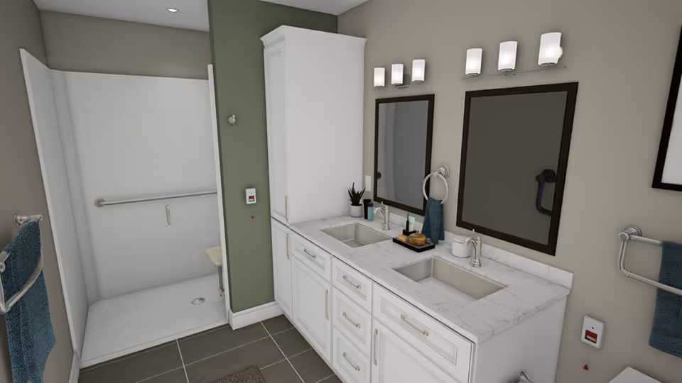 A modern bathroom with a double sink vanity featuring white cabinets and marble countertops. Two rectangular mirrors with dark frames are mounted above the sinks, each with a light fixture above. To the left, there is a walk-in shower with a white tiled wall, a grab bar, and a fold-down seat. Blue towels hang on towel racks on both sides of the vanity. The walls are painted in a combination of light beige and green, and the floor is covered with large gray tiles.