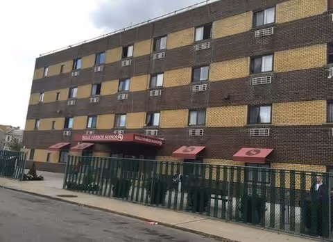 Exterior view of a multi-story brick senior living building with red awnings and a green gate.
