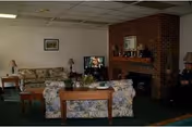 Shared lounge with floral sofas, wooden tables, a brick fireplace, and a television.