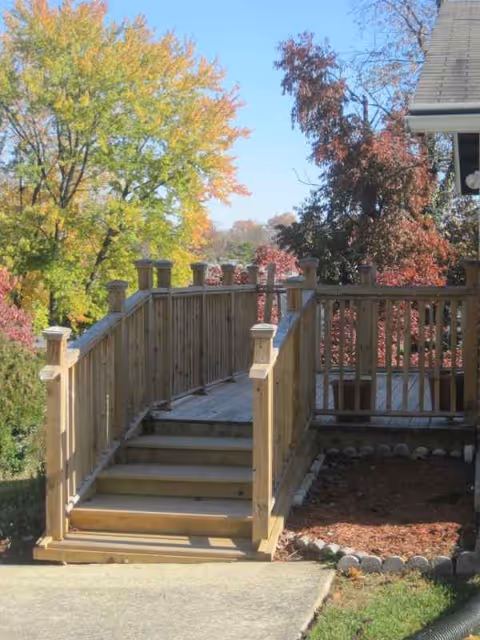 Wooden deck with stairs and railing outside a building amid colorful autumn trees.