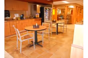 Small dining area with round tables and chairs in front of a kitchenette and a vending machine.