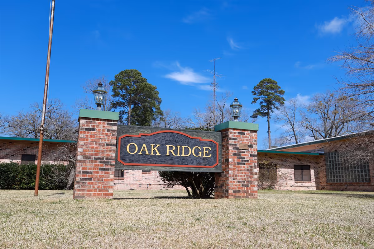 Outdoor view of the Oak Ridge Health & Rehab facility sign mounted on two brick pillars with lamps on top, set on a grassy lawn with trees and a clear blue sky in the background.
