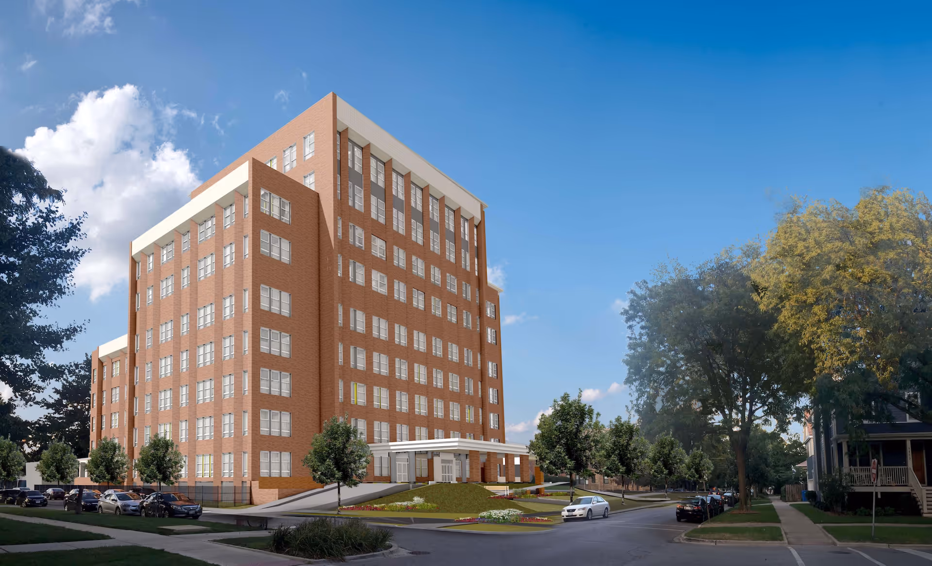 Exterior view of a multi-story brick building with many windows, surrounded by trees and parked cars on a street under a blue sky with some clouds.