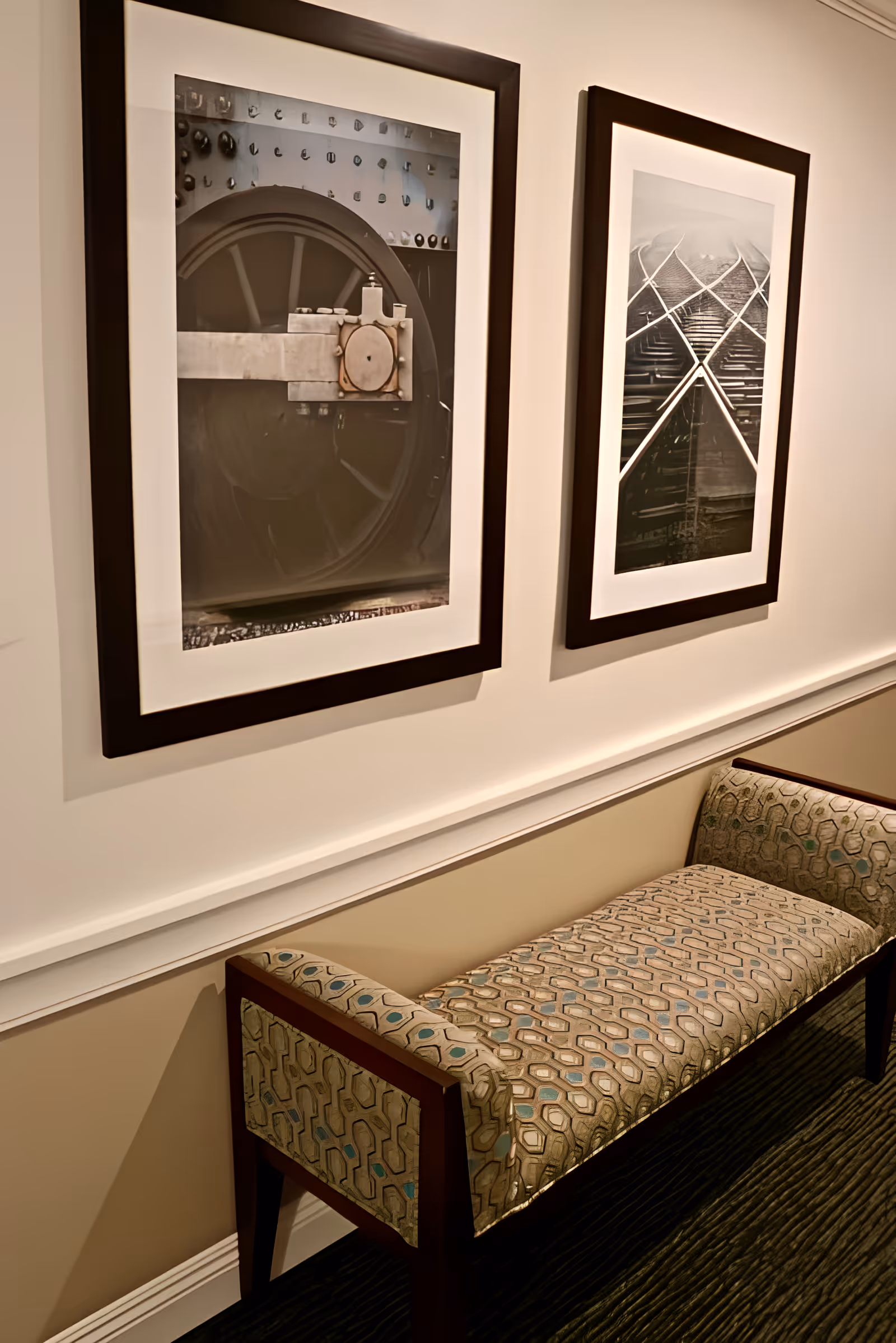 A patterned upholstered bench sits against a hallway wall beneath two framed black-and-white photographs.