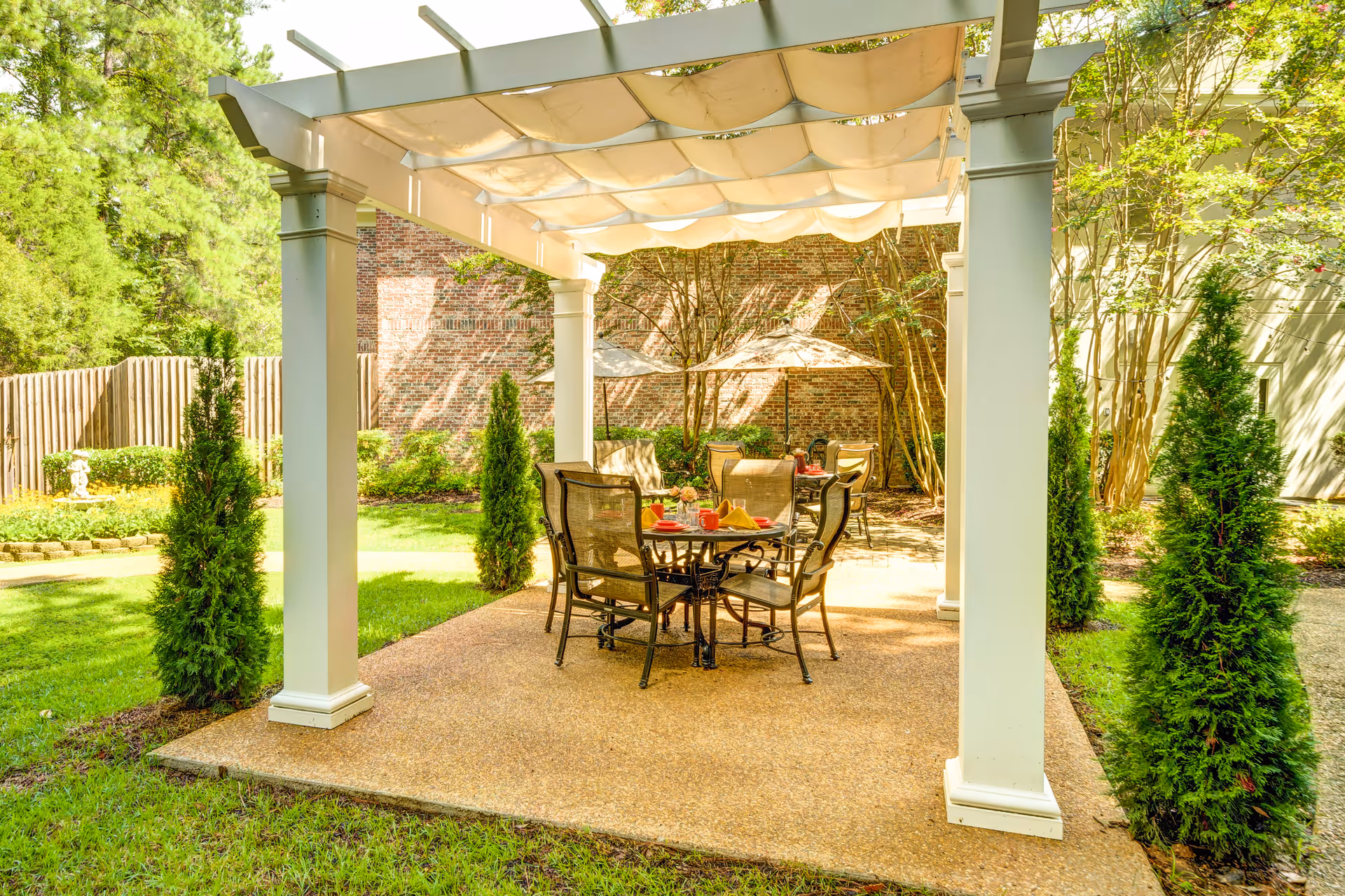 A serene outdoor patio area at Castlewoods Place featuring a table with chairs, surrounded by greenery and decorative plants.