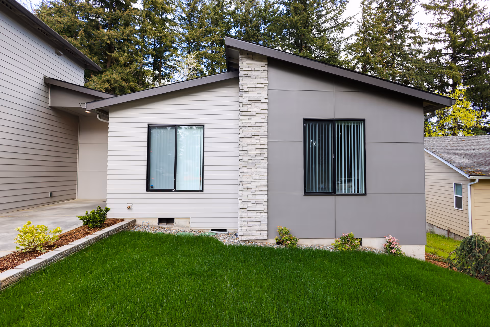 Front exterior of a modern single-story house with two windows, a stone column, and a green lawn.