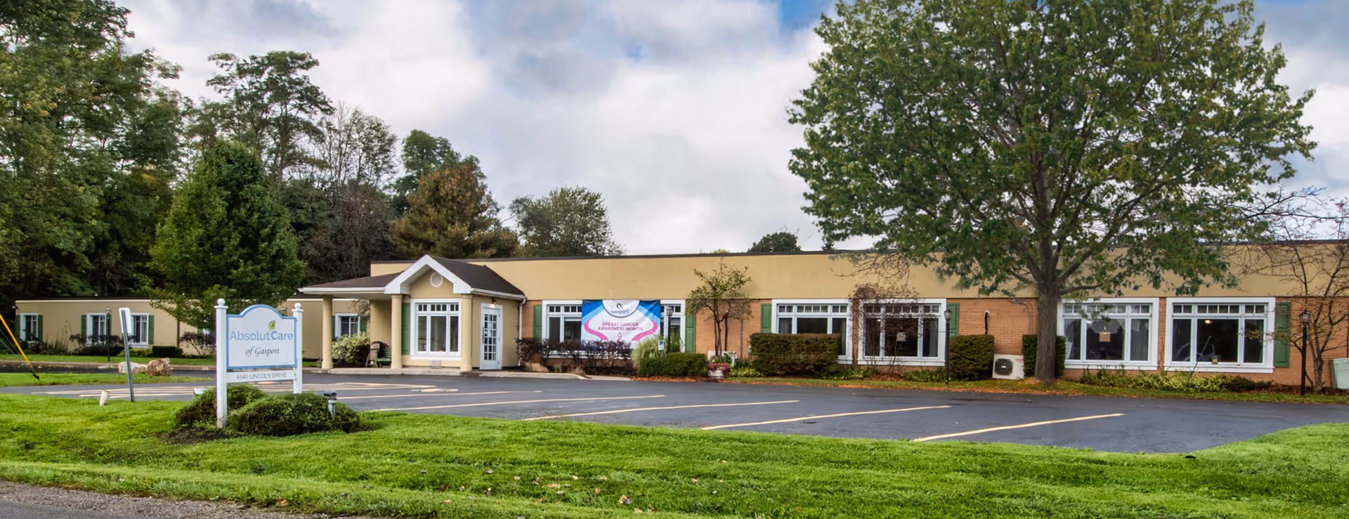 Single-story senior living facility labeled "Absolut Care of Gasport" with a front lawn, parking lot and main entrance.