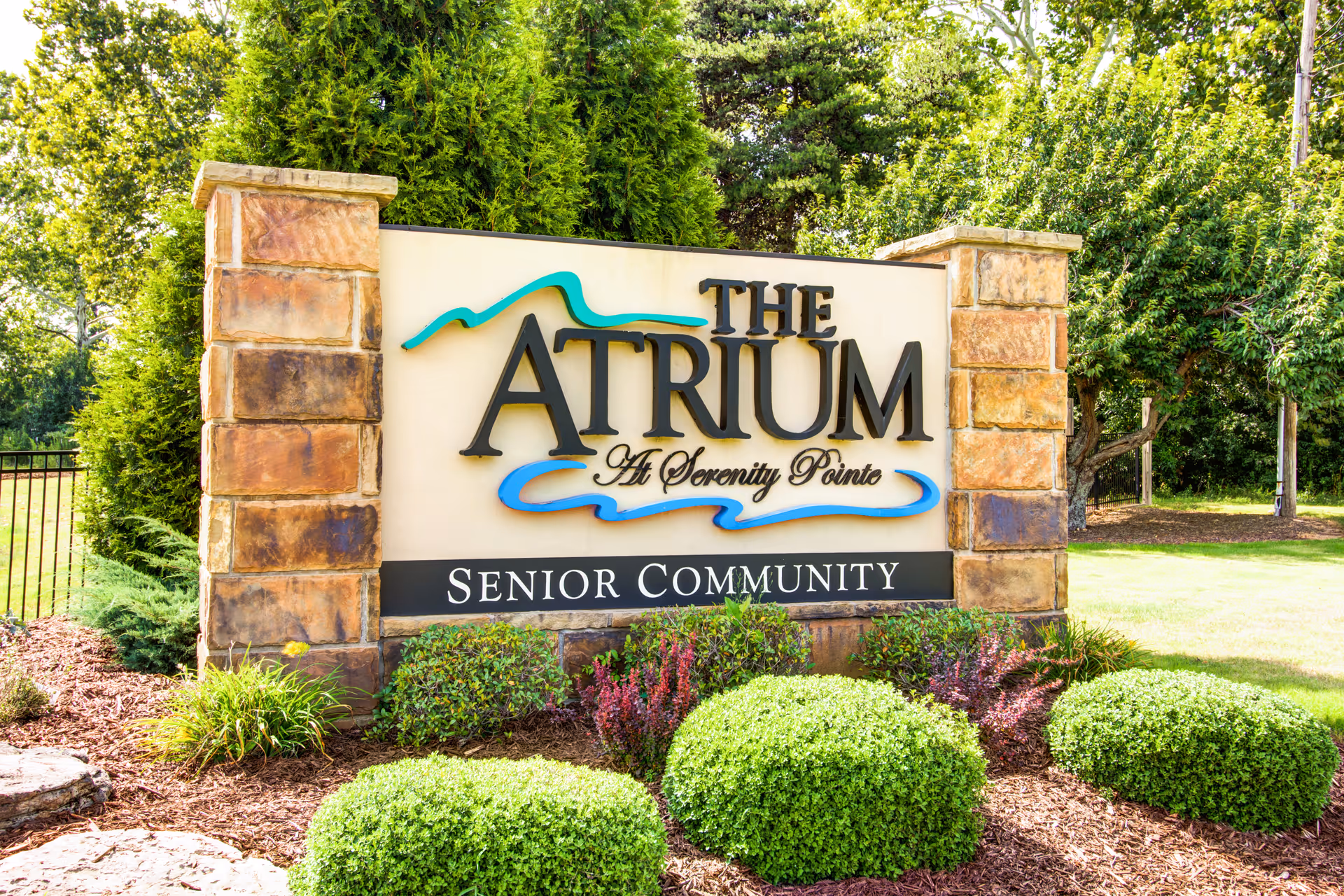 Stone entrance sign reading 'The Atrium At Serenity Pointe Senior Community' set among landscaped bushes and trees.