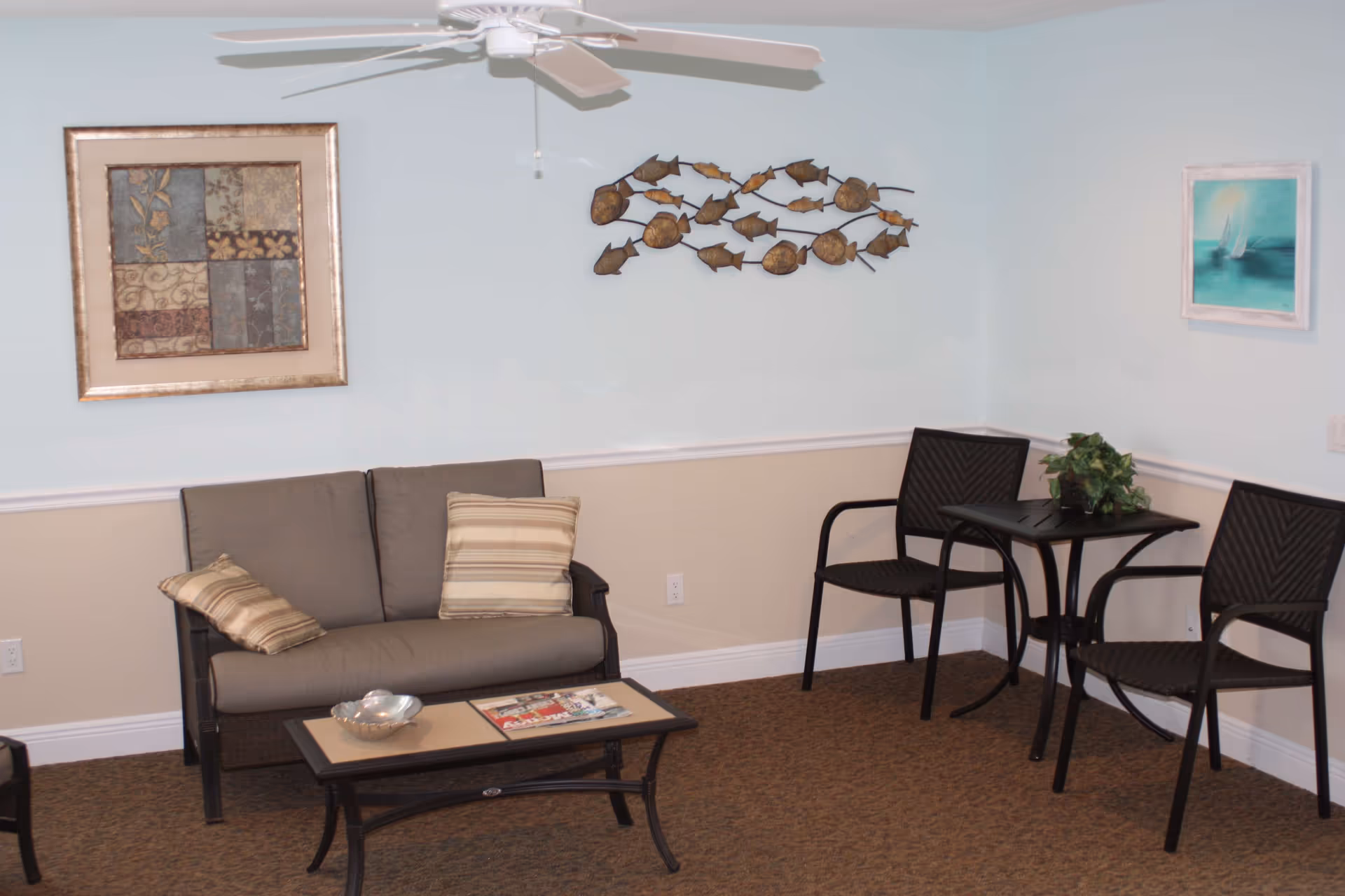 Small seating area with a loveseat, coffee table, two chairs and a small table against a pale blue wall with decorative wall art.