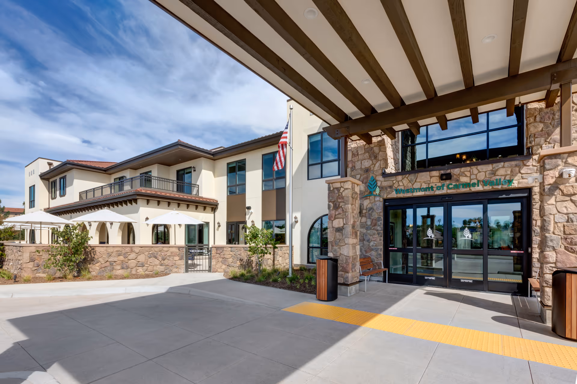 Exterior view of Westmont of Carmel Valley entrance with stone facade, glass doors, and flag.