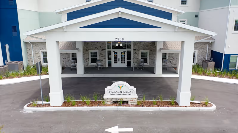 Covered front entrance and drop-off area of Sunflower Springs at Trinity with the facility sign and building façade visible.