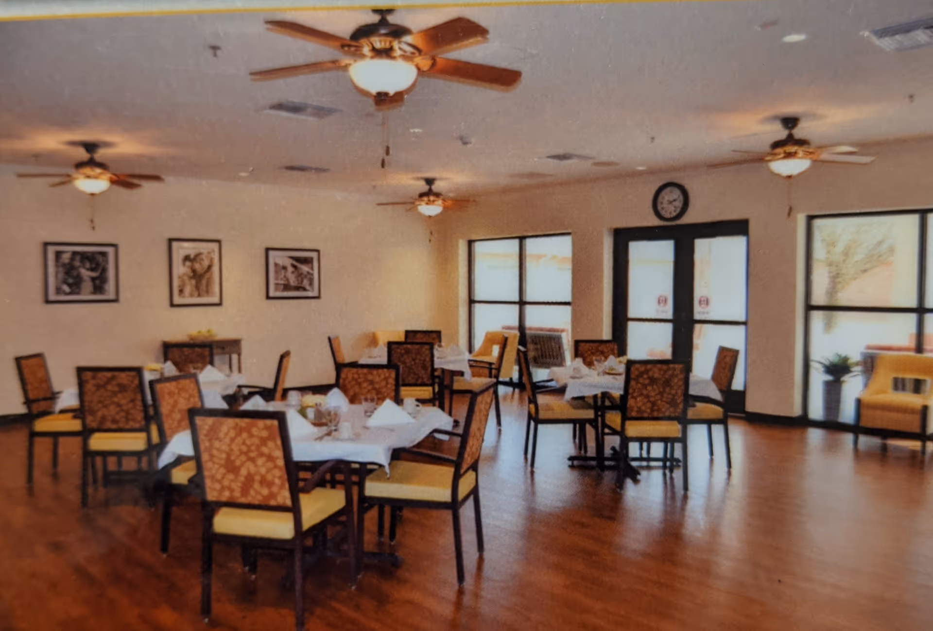 Dining room with multiple set tables and patterned chairs, ceiling fans, large windows and double doors.