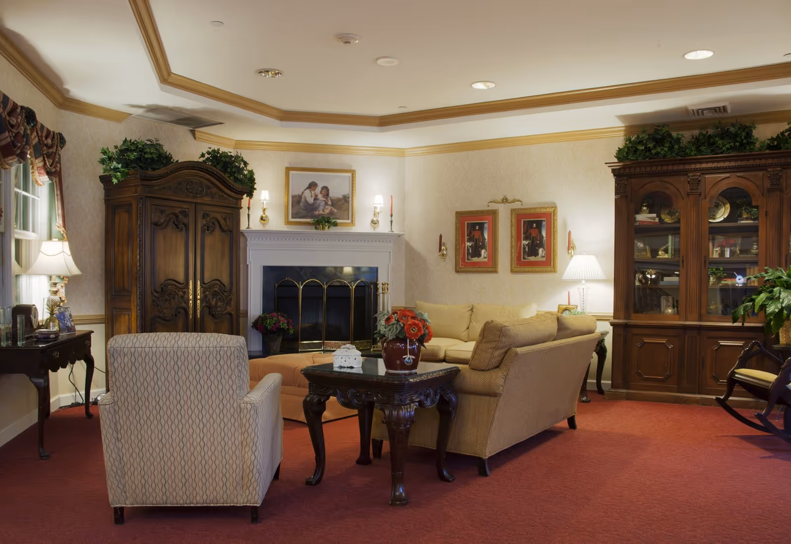 A cozy living room with sofas and armchairs arranged around a coffee table and fireplace, flanked by ornate wooden cabinets and lamps.
