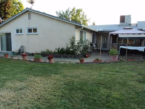 Exterior view of The Heights Care Home with lawn, potted plants, and a covered patio.