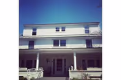 Two-story white building with a covered front porch and rails.