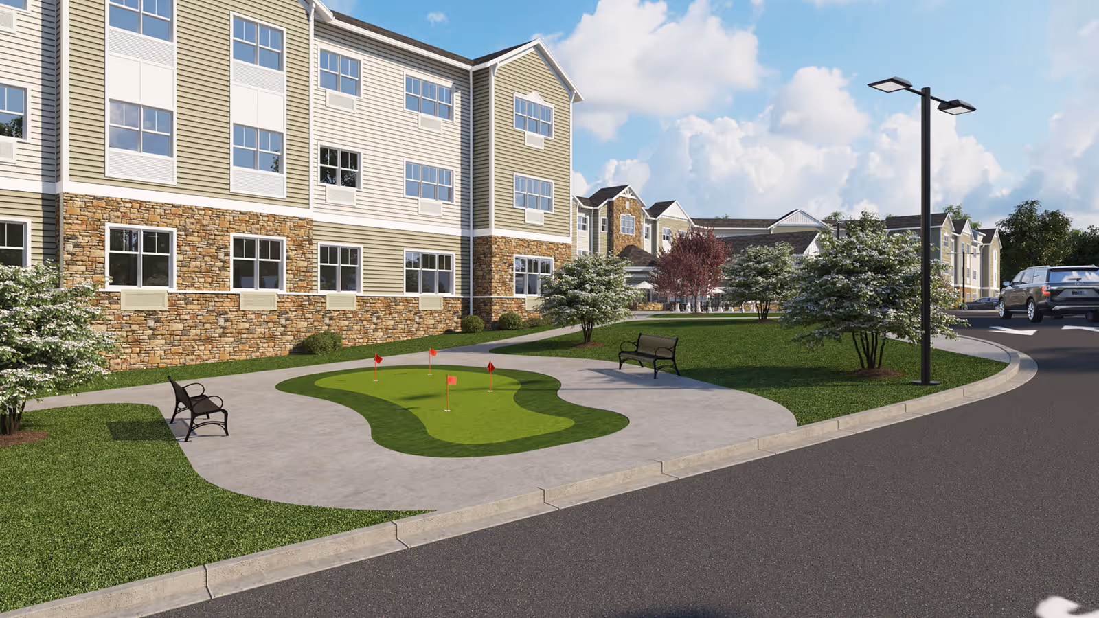 Front exterior of a multi-story senior living building with a small putting green, benches, and landscaped lawn.