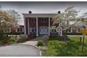Residential-style brick facility with white columns, green lawn, and curved driveway at the entrance.