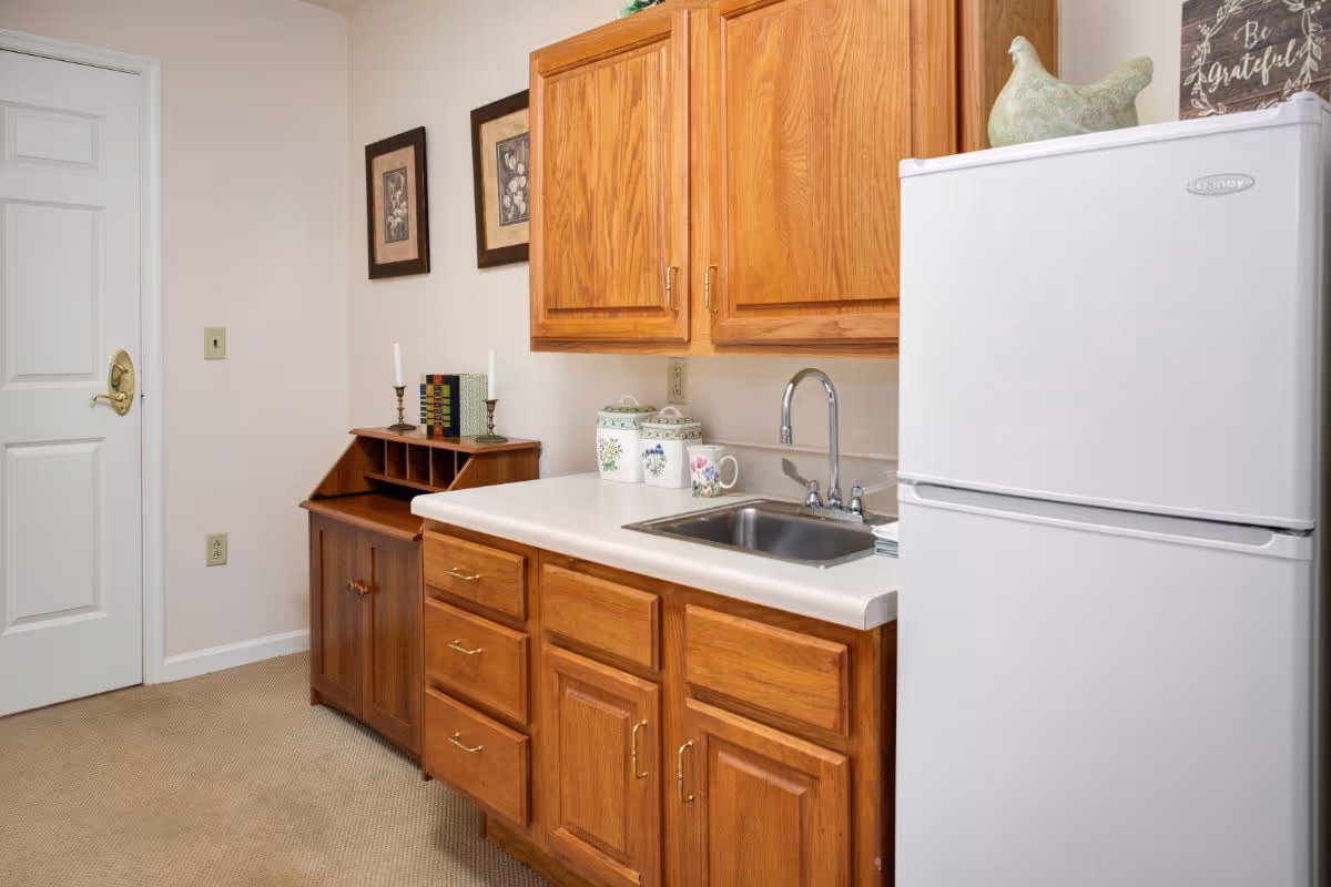 Small kitchenette with wooden cabinets, a sink, countertop decor, and a white refrigerator.