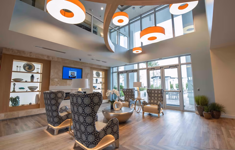 Spacious modern lobby seating area with patterned armchairs, large windows and hanging circular lights.