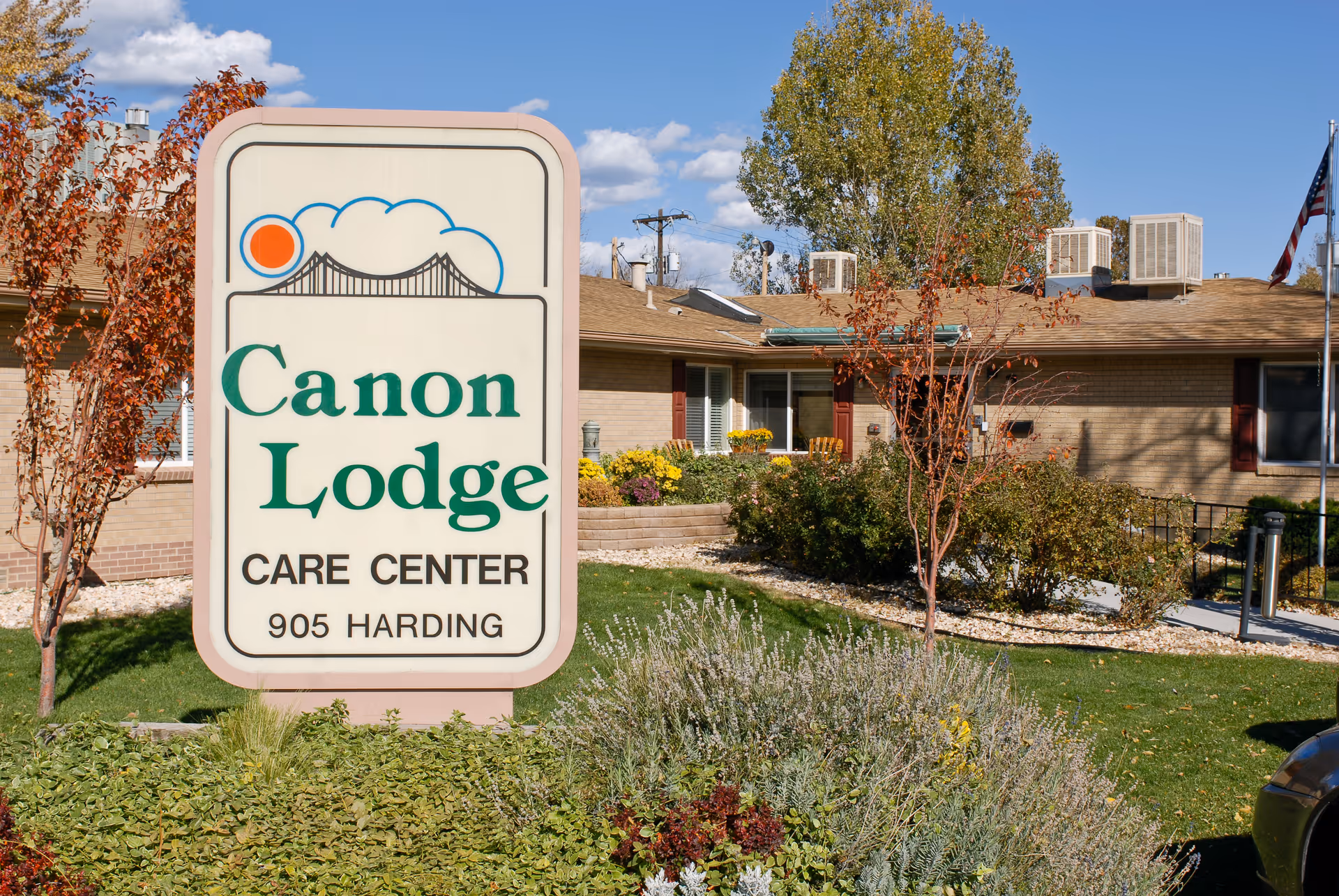 Outdoor view of Canon Lodge Care Center sign with the building and landscaping in the background under a blue sky with some clouds.