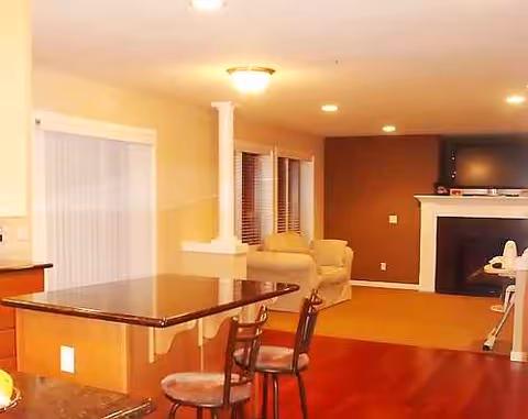 Bright living room in a senior care center with sofa, fireplace, and dining counter.