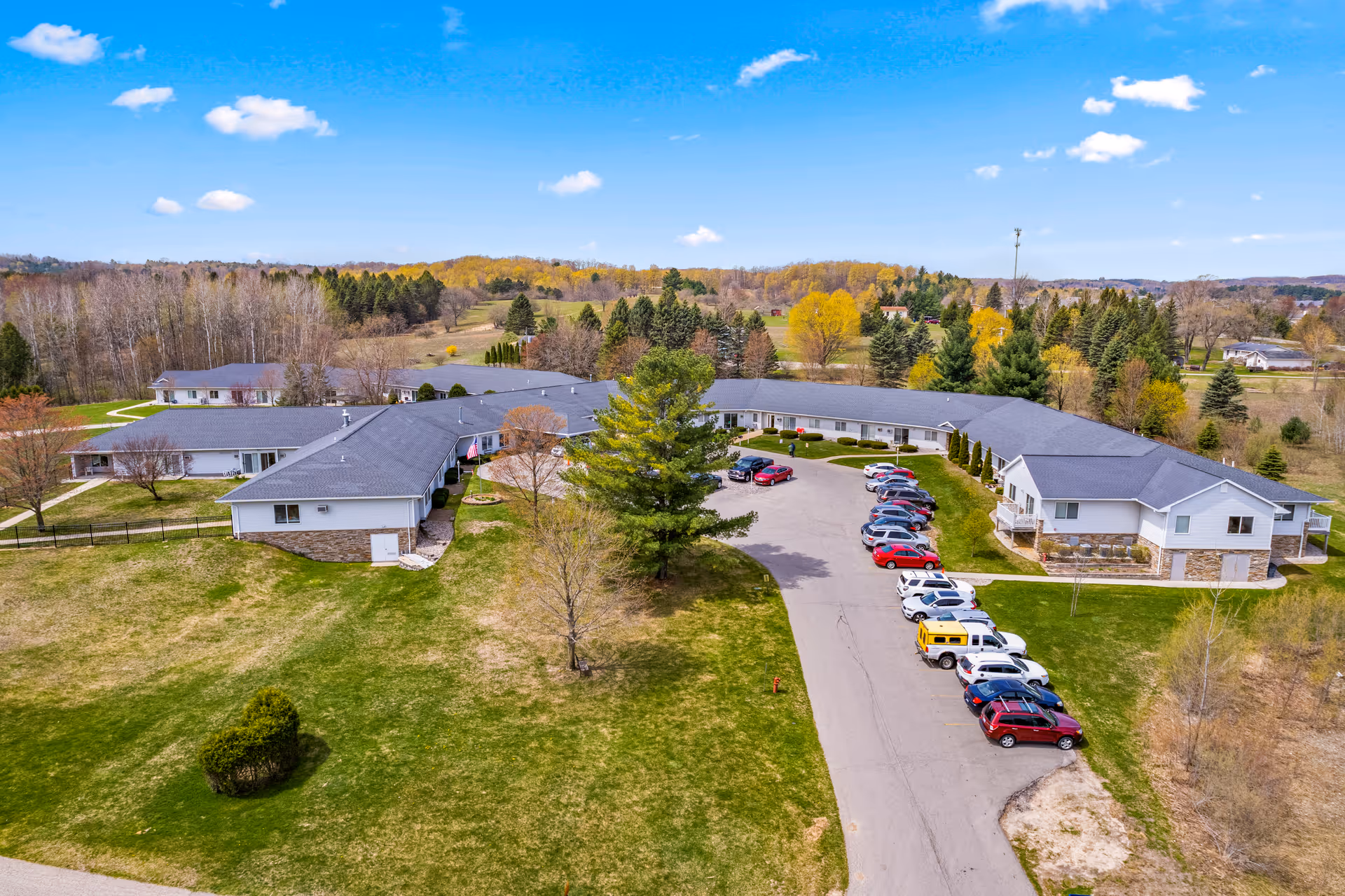Aerial view of a single-story senior living complex with curved buildings, a parking lot, and surrounding lawns and trees.