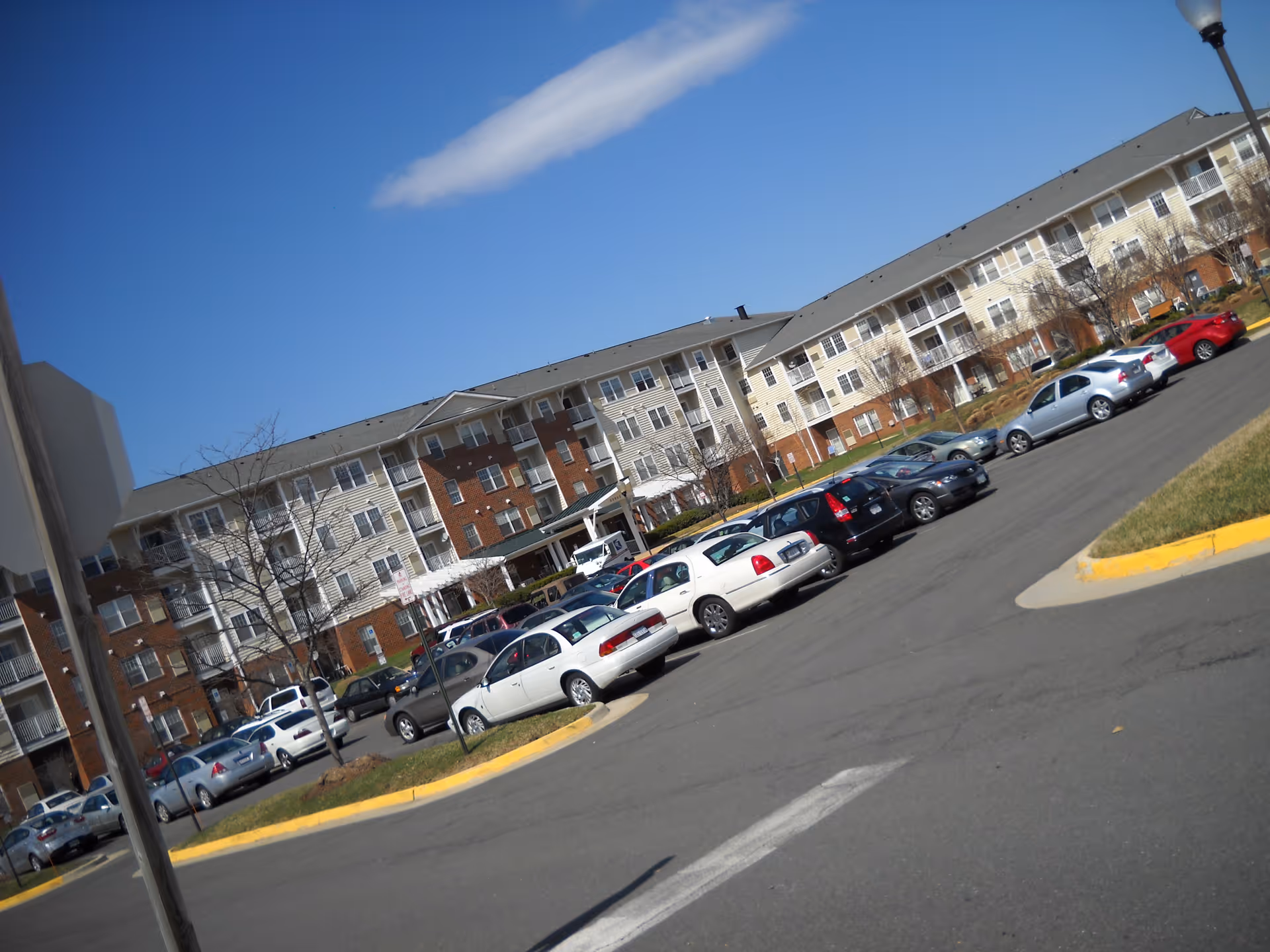 Parking lot with multiple cars in front of a large multi-story residential building under a clear blue sky.
