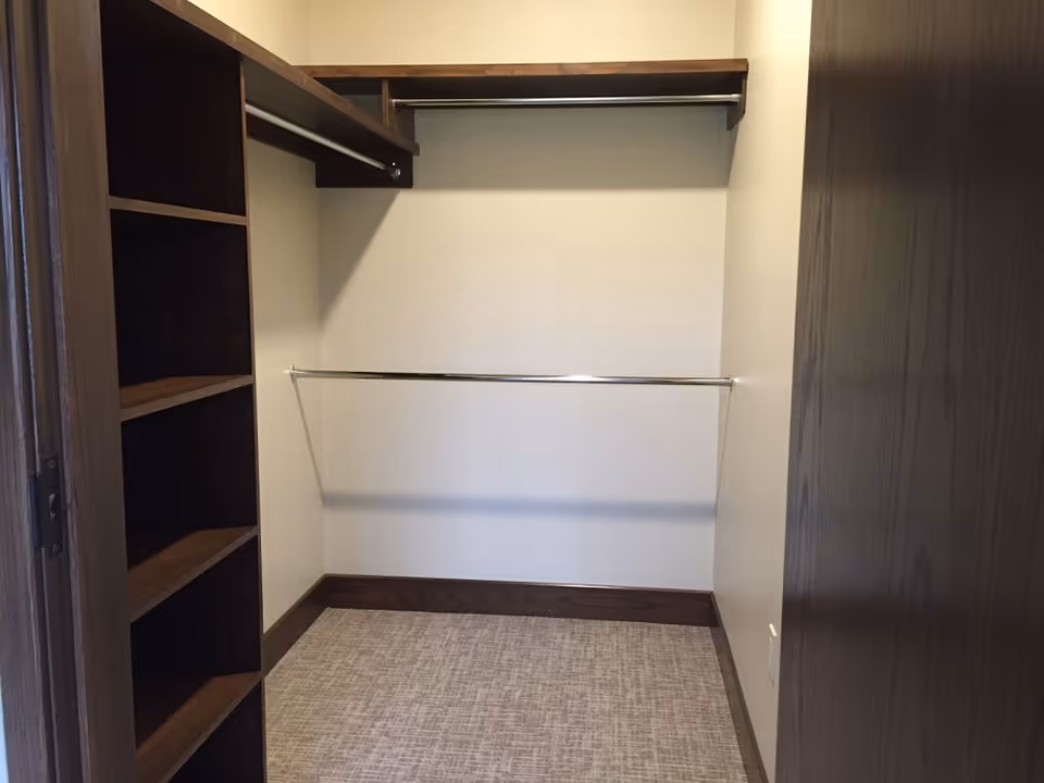 Empty walk-in closet with built-in dark wood shelves, two metal hanging rods, and a carpeted floor.