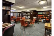 Well-lit library-style common room with bookshelves, upholstered chairs, and small tables.