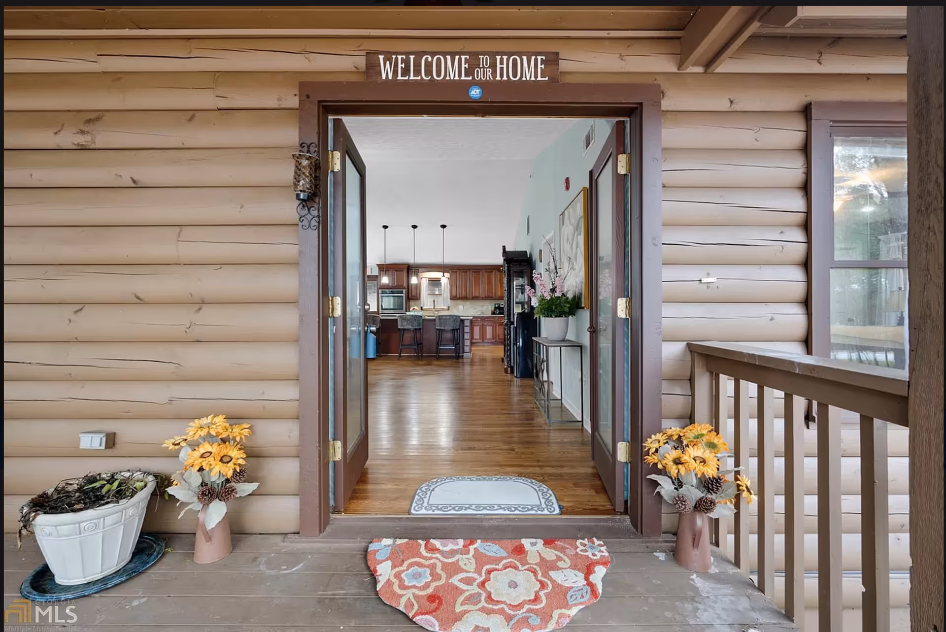 Front porch with open double doors revealing a home interior and kitchen with hardwood floors.