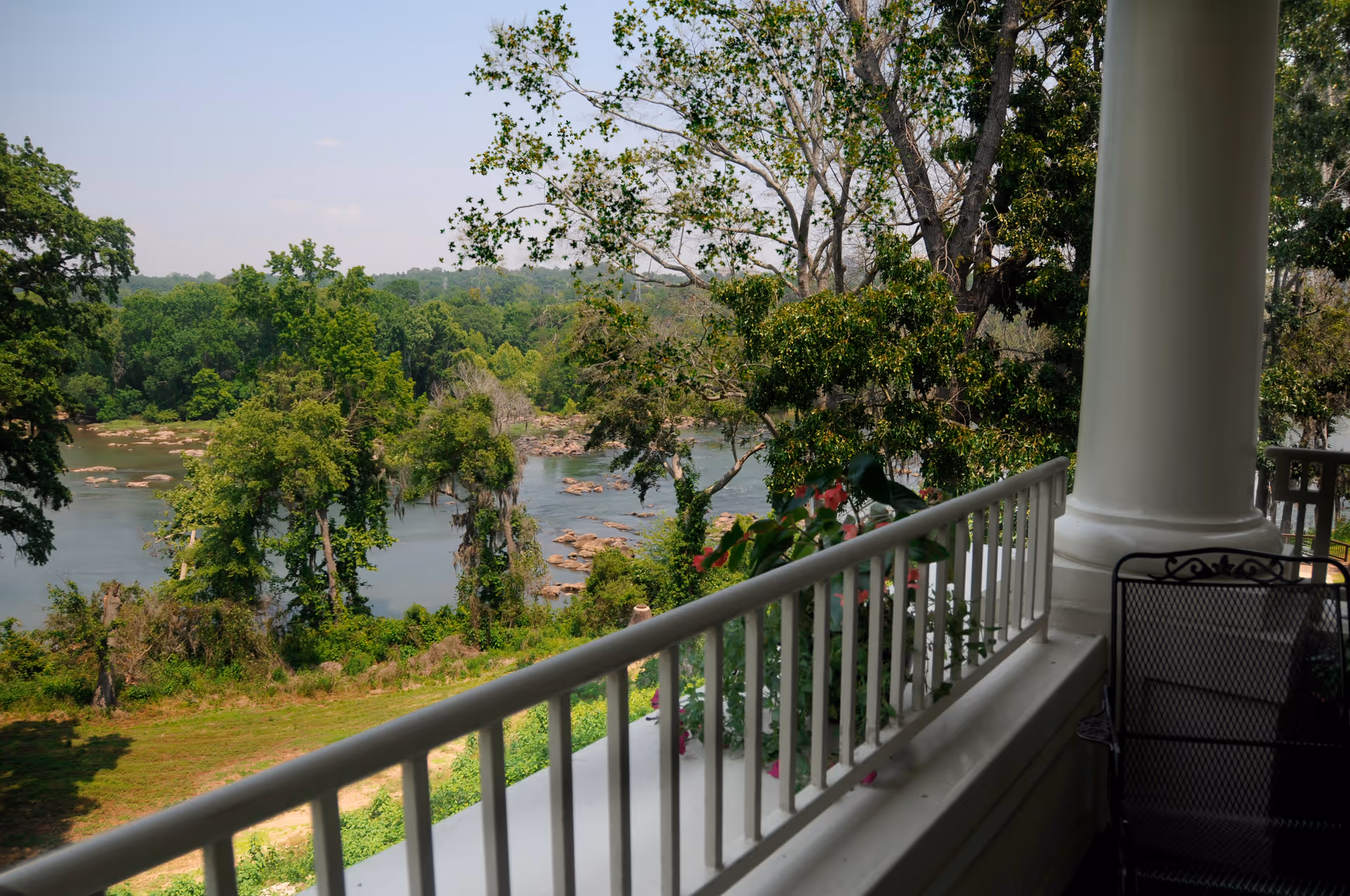 View from a porch with a white railing and column overlooking a river and wooded shoreline