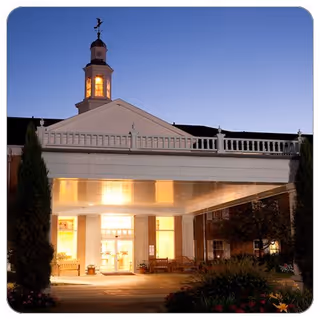 Front entrance of a senior living facility at dusk with a lit porte-cochère and cupola.