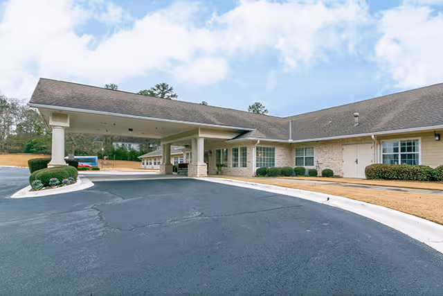Front entrance of a single-story senior living facility with a covered porte-cochère and paved driveway.