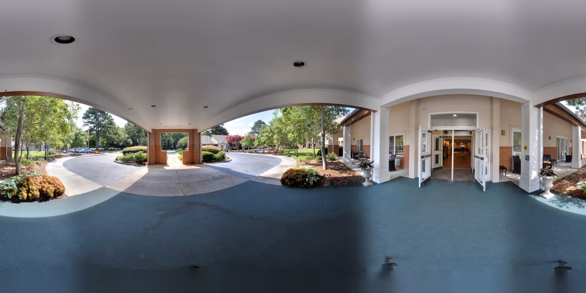 Covered porte-cochere and main entrance of Savannah Square with a circular driveway, landscaping, and open double doors.