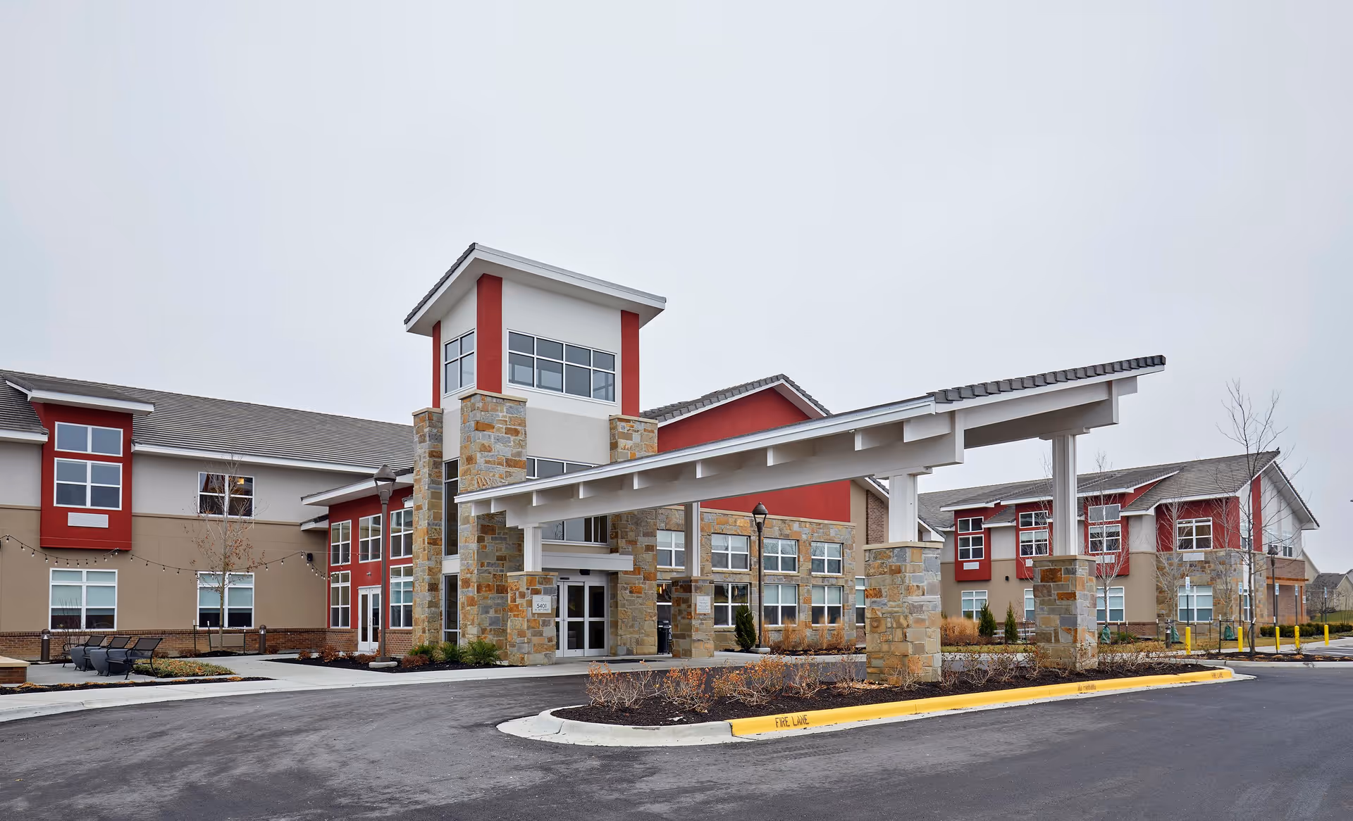 Exterior view of Leawood nursing home building with a covered entrance supported by stone pillars, multiple windows, and a paved driveway with landscaping around the entrance.