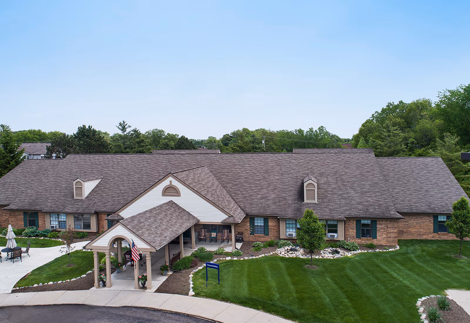 Single-story brick senior living building with a covered entrance, American flag, and manicured lawn.