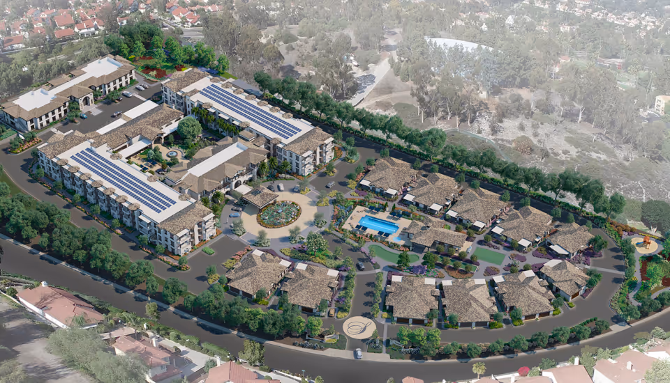 Aerial view of Silvergate Rancho Bernardo senior living facility showing multiple buildings with brown roofs arranged around a central circular driveway with landscaped gardens. The complex includes a swimming pool, walking paths, and abundant greenery with trees and shrubs. Surrounding the facility are residential neighborhoods and natural wooded areas.