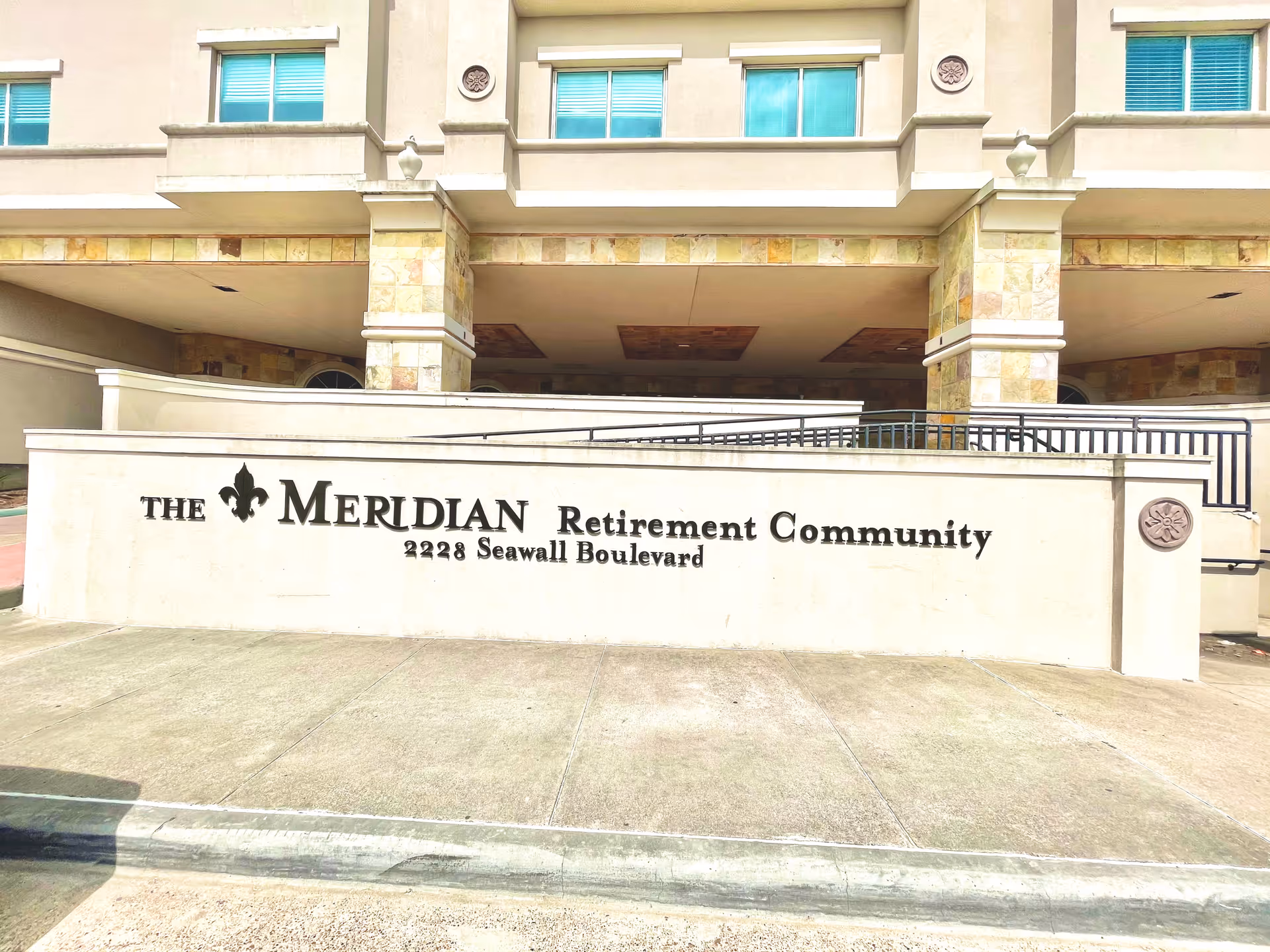 Exterior view of the entrance sign for The Meridian Retirement Community located at 2228 Seawall Boulevard, with part of the building facade visible in the background.