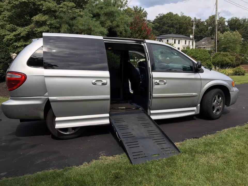 Silver wheelchair-accessible van with side ramp extended on a driveway.