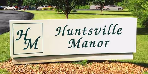 A large white sign reading Huntsville Manor with a green logo sits on a landscaped lawn.