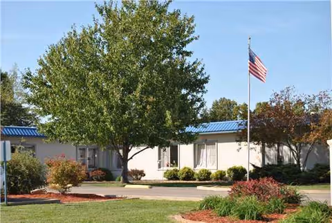 Exterior view of Camdenton Windsor Estates with trees, shrubs, and an American flag.