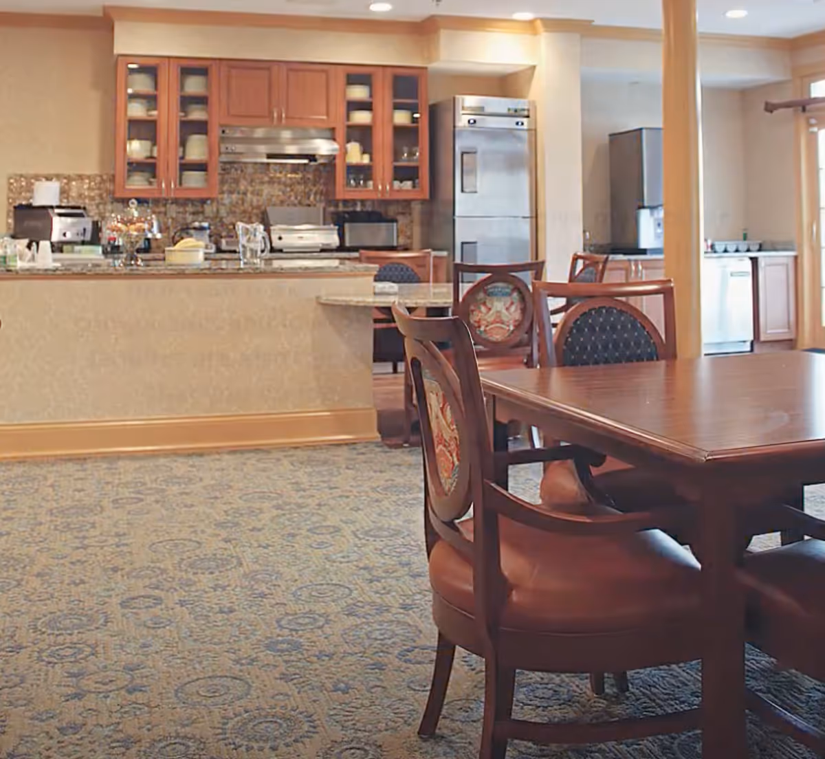 Dining area with wooden table and chairs in front of a kitchen counter and cabinetry.