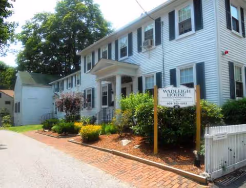 Two-story white building with blue shutters, front entrance, and landscaped walkway.