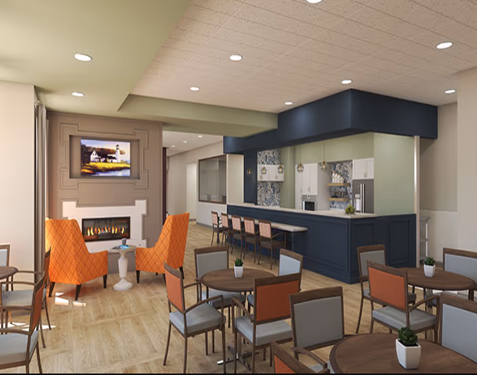 Bright communal dining and lounge area with round tables and chairs, a fireplace with a TV above, and a long bar/kitchen counter.